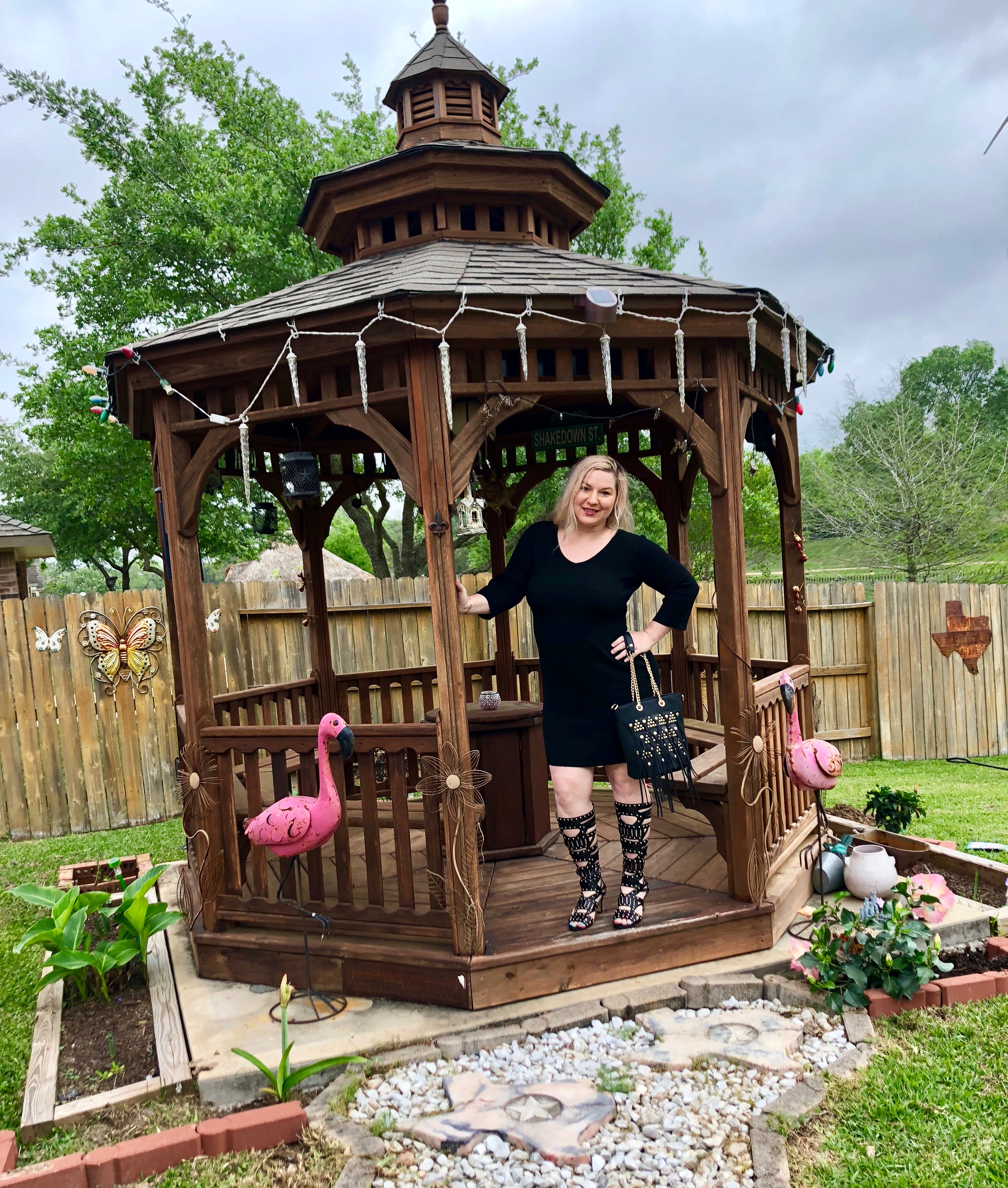 A Midnight Velvet customer in a gazebo, wearing a black dress, tall black studded boots, with a matching bag.