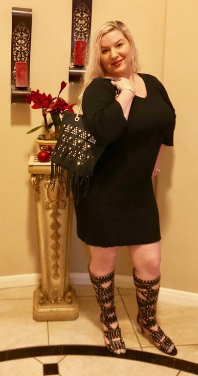 A Midnight Velvet customer in a round foyer, wearing a black dress, tall black studded boots, with a matching bag.