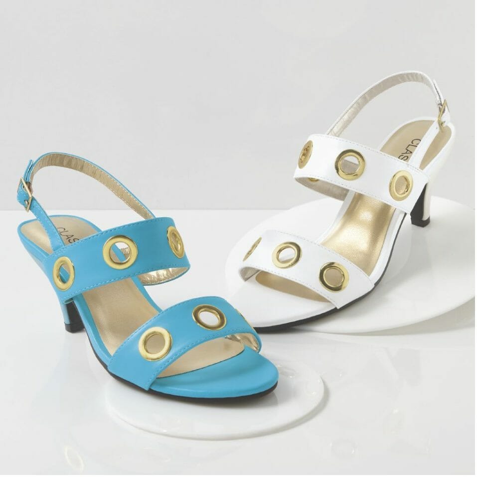 Two low-heeled sandals with back buckle strap and wide gold grommets on the two bands, one in white and one in turquoise.