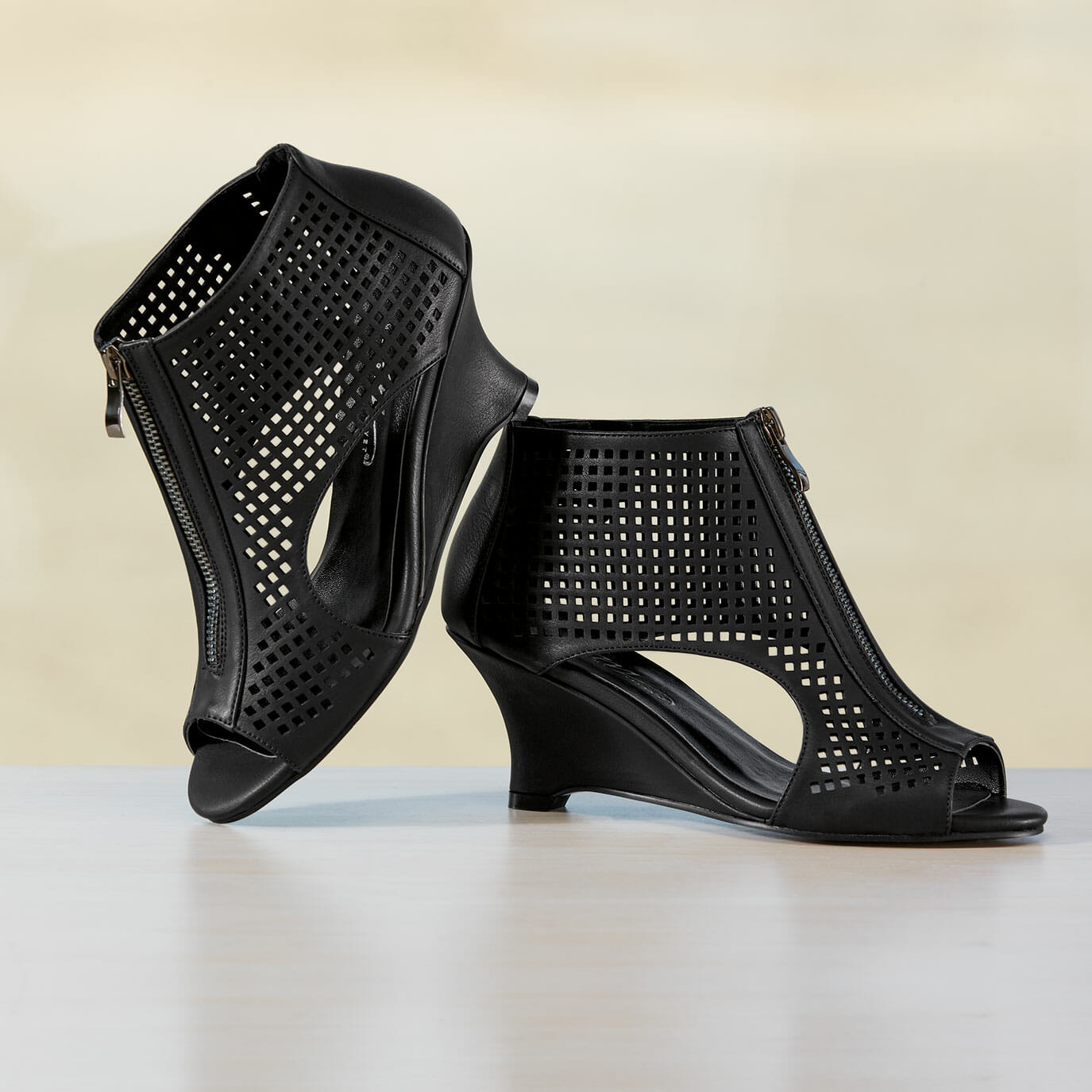 Black faux leather gladiator shoe with a wedge heel, open toe and lower sides, front zipper and pierced sides.