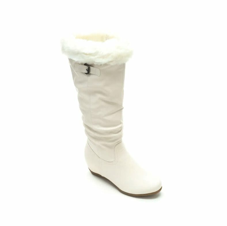 A tall, flat ivory faux leather boot with a white faux fur cuff and a decorative upper brass buckle.