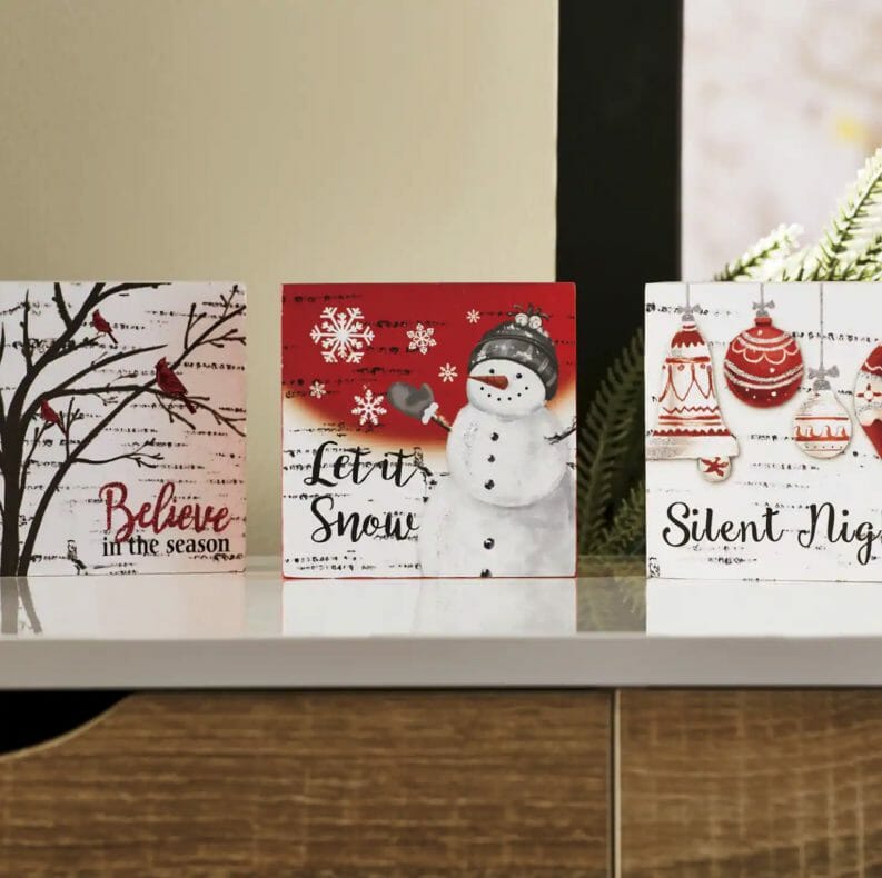 Three white, red, and black print Holiday cards on a shelf, including Believe in the Season, Let it Snow, and Silent Night.