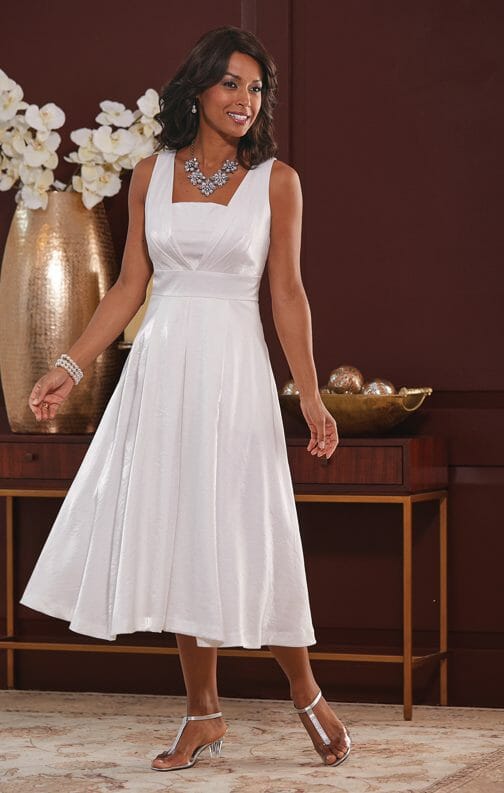 An African-American woman in a formal white sleeveless dress with a full skirt, silver sandals and a crystal necklace.